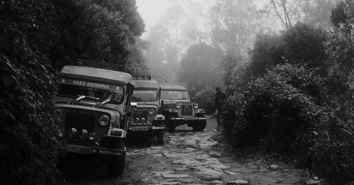 Black and white image of jeeps on a foggy road in Munnar, India, showcasing rugged terrain.